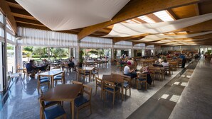 An indoor dining area with wooden tables and chairs, large windows, and a high ceiling with exposed beams. - Aparthotel Ciudad Laurel (Son Servera)