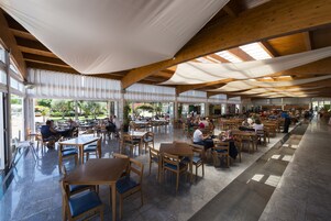 Un comedor interior con mesas y sillas de madera, ventanas amplias y un techo alto con vigas a la vista.