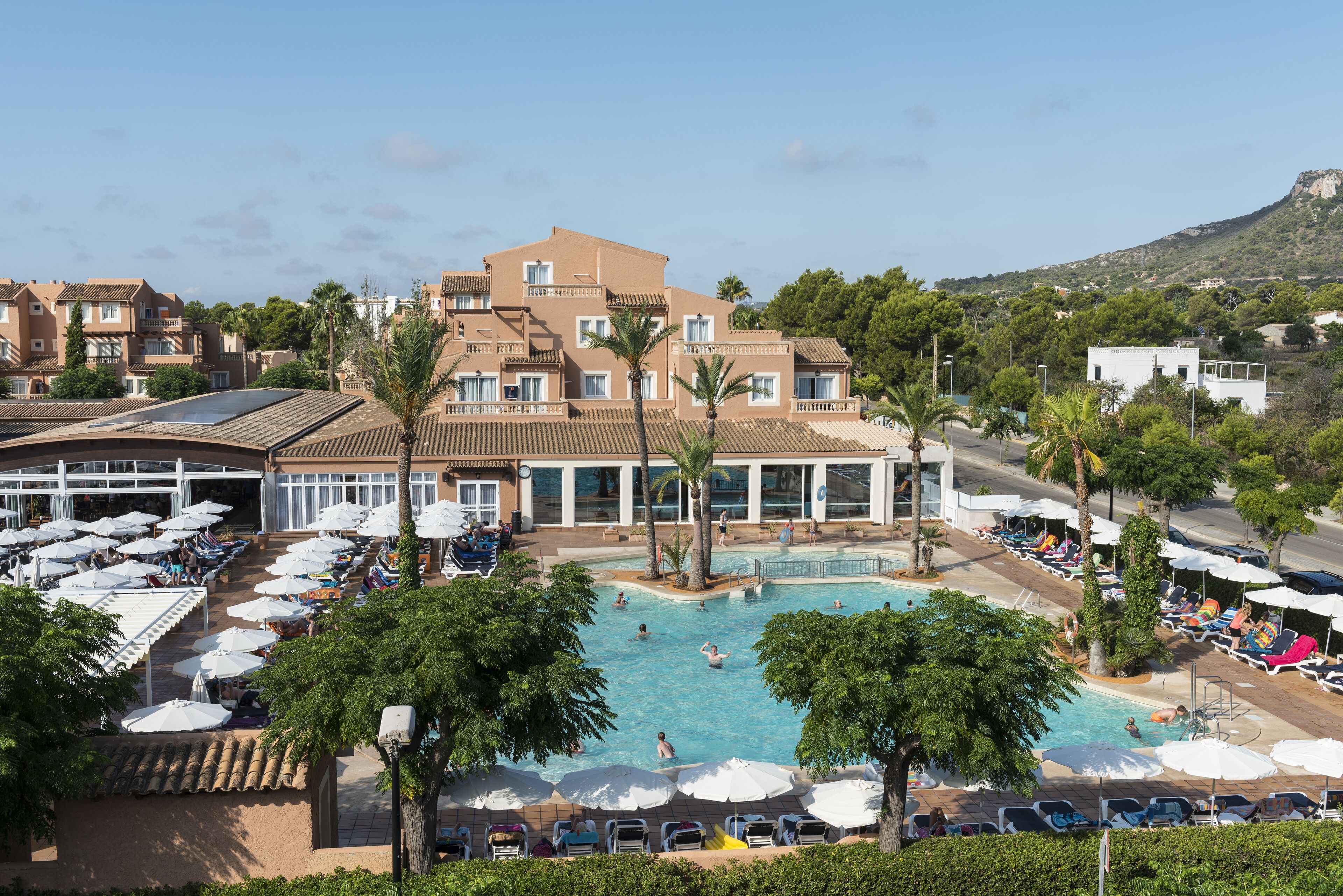 Un hotel con piscina rodeada de palmeras y tumbonas.