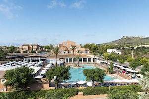 Un resort con una piscina grande, varias zonas de descanso y vistas a una colina.