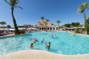Una amplia piscina al aire libre rodeada de palmeras y sillas de descanso.