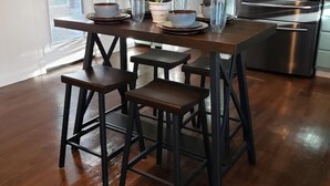 A modern kitchen with a stainless steel refrigerator, wooden bar stools, and a dining table set for four. - 🧜‍♀️ Oasis Paradise Guesthouse (Granbury)