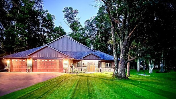 Une maison à deux étages avec un garage, une pelouse bien entretenue et un grand arbre dans le jardin.