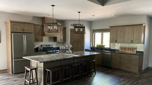 Une cuisine moderne avec des meubles en bois, un réfrigérateur en acier inoxydable, un grand îlot central doté de tabourets et un éclairage suspendu.