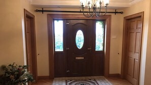 A wooden front door with a glass panel, a chandelier, and a patterned rug on a wooden floor. - Dungannon 2 Bed Bungalow - Sleeps 5 - Pet Friendly (Dungannon)