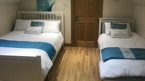 A bedroom with two beds, a wooden door, and a painting on the wall. - Dungannon 2 Bed Bungalow - Sleeps 5 - Pet Friendly (Dungannon)