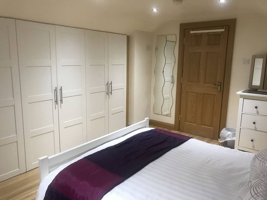 A bedroom with a large wardrobe, a wooden door, a dresser, and a bed with a patterned bedspread.