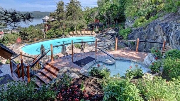 Piscina con cubierta de madera y escaleras, rodeada de abundante vegetación y vistas a un lago.