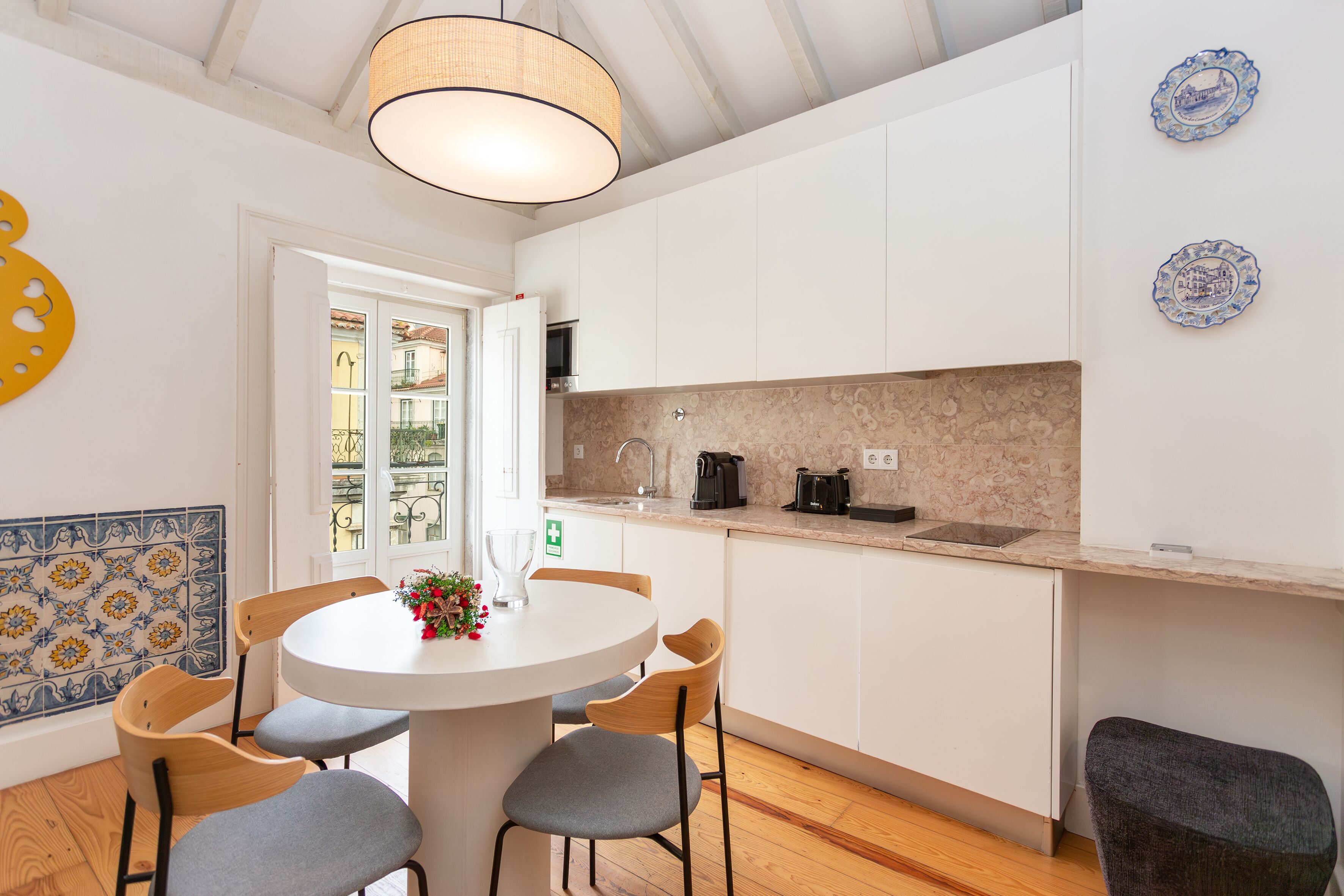 Une cuisine moderne avec des meubles blancs, une table de salle à manger ronde entourée de chaises et un luminaire suspendu.