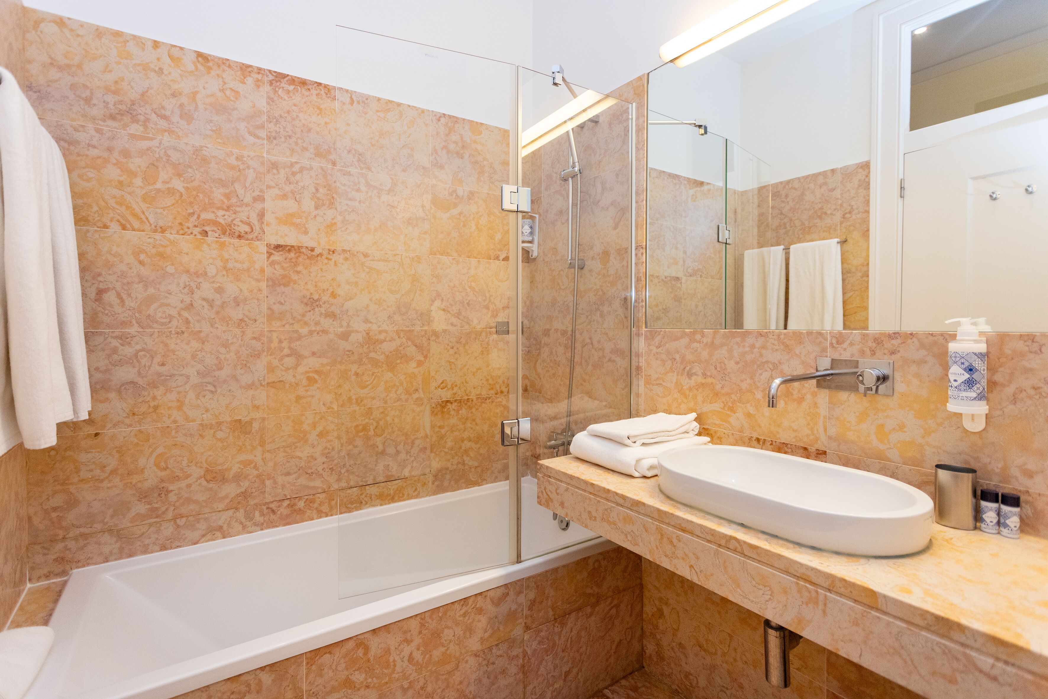 A bathroom with a bathtub, a glass-enclosed shower, a sink with a mirror, and a towel rack.