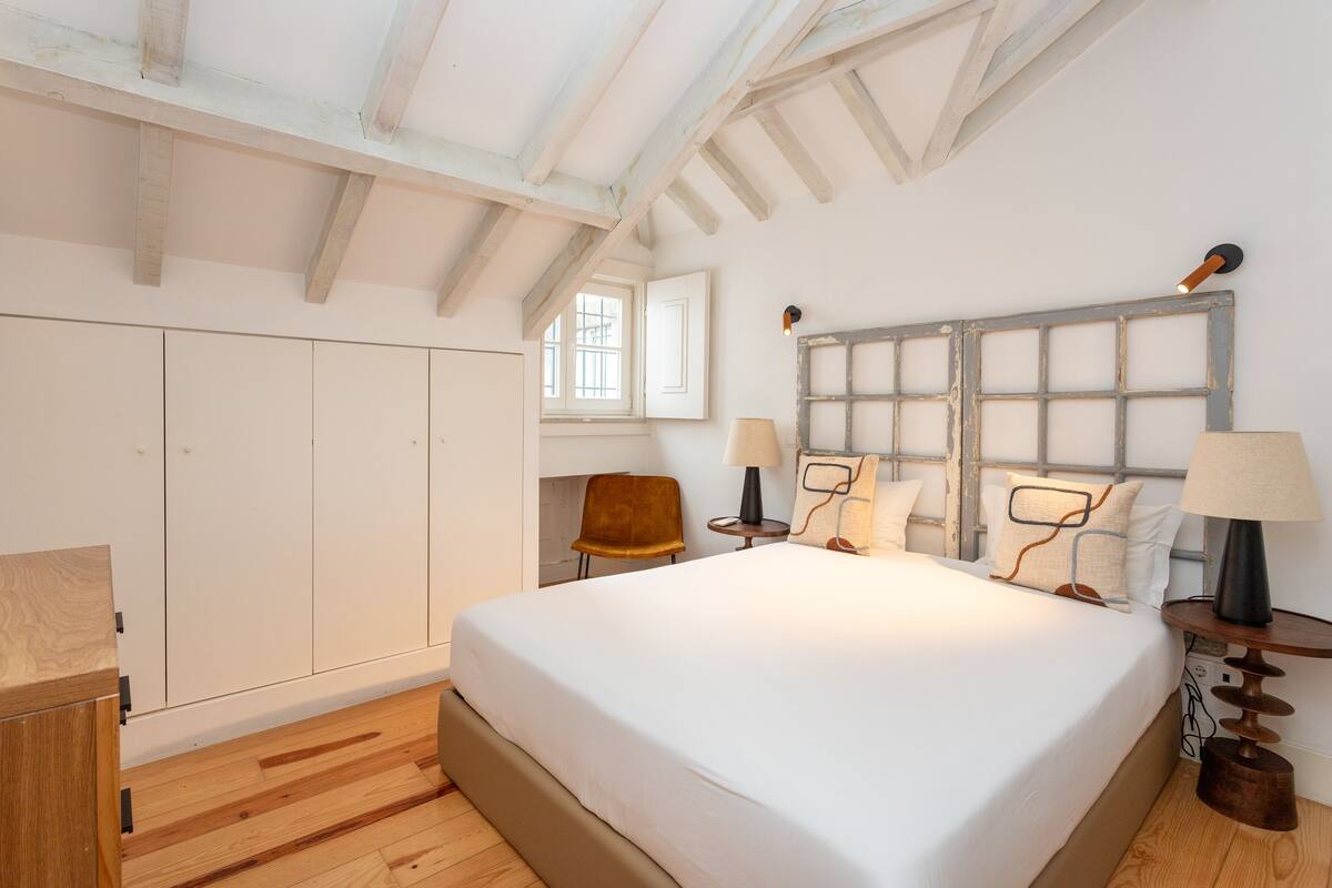 A bedroom with a large bed, wooden wardrobe, and a window.