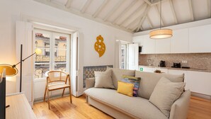 A modern living room with a sofa, a chair, a lamp, and a kitchen area with cabinets and a countertop. - Casas da Baixa - Jules & Madeleine (Lisbon)