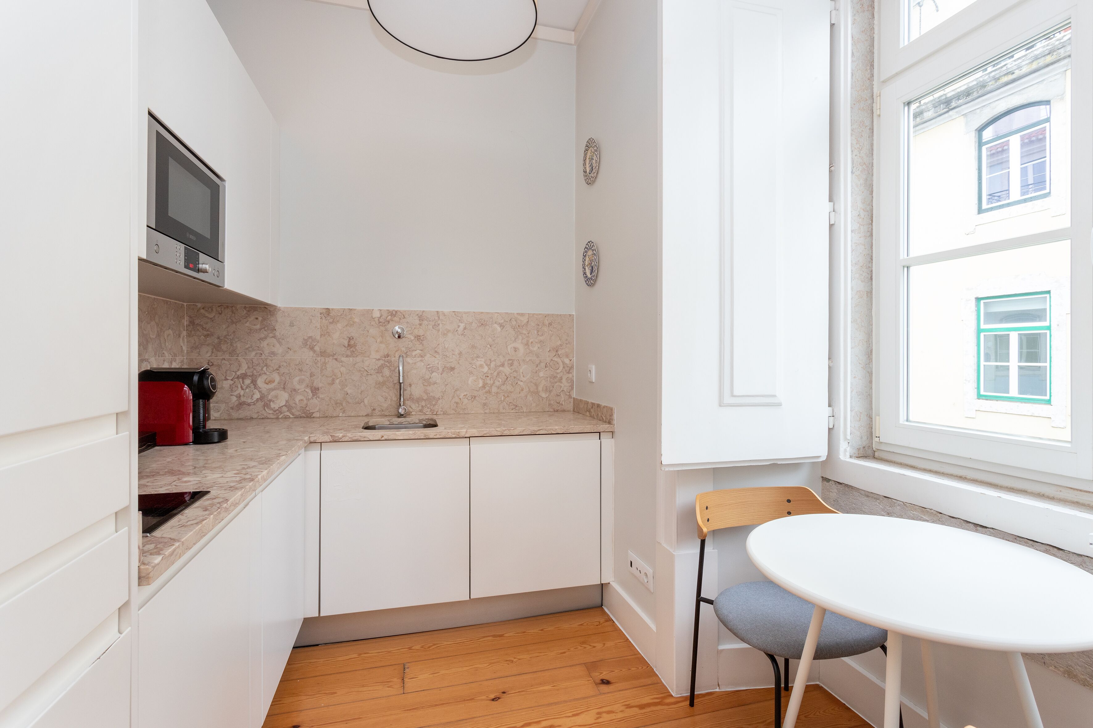 A compact kitchen with white cabinets, a microwave, a sink, and a small table with a chair.