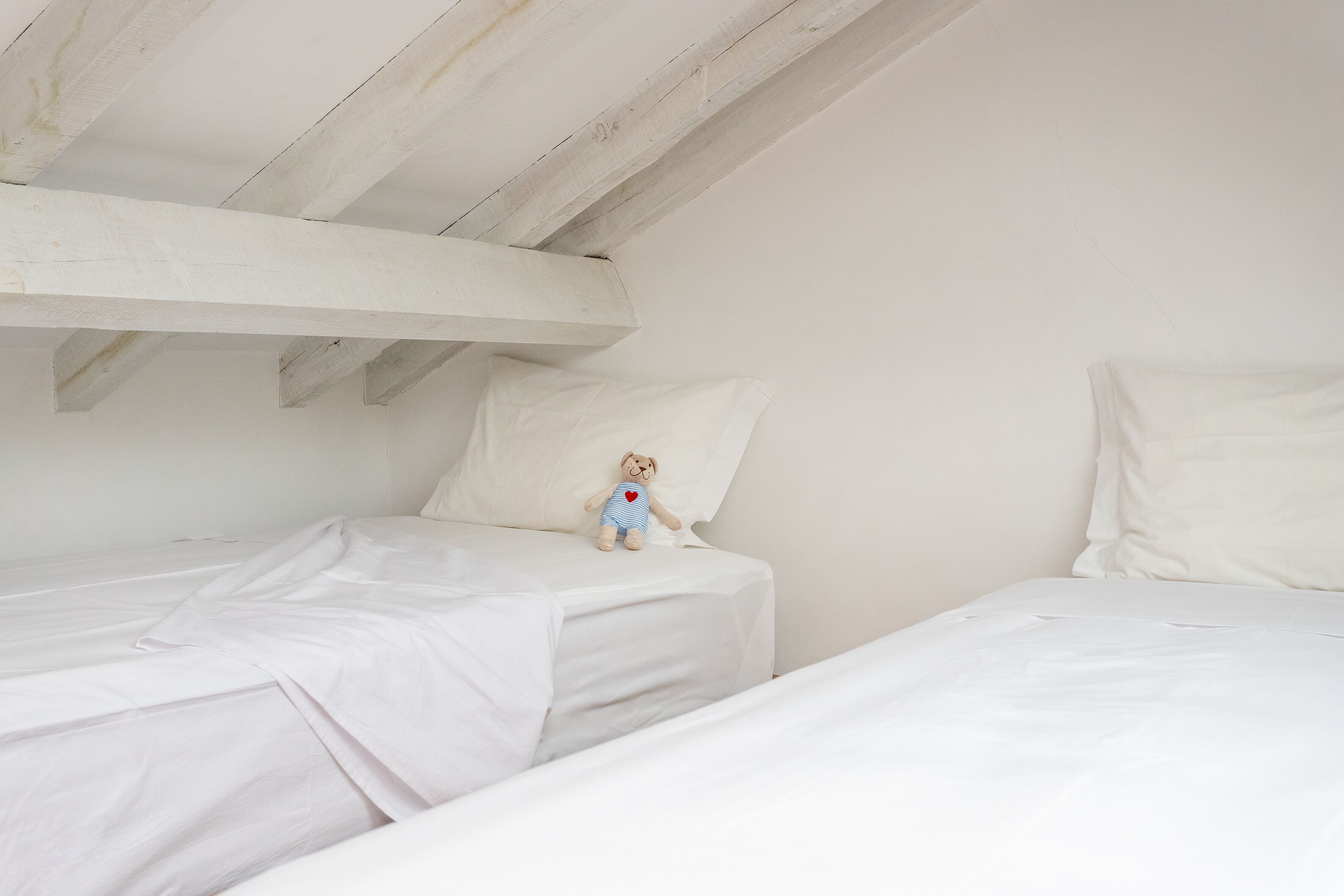 A bedroom with two single beds, white bedding, and a teddy bear on one bed.