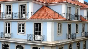 A multi-story building with a red-tiled roof, balconies with wrought iron railings, and a light blue facade. - Casas da Baixa - Jules & Madeleine (Lisbon)