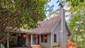 Une maison de plain-pied avec un toit à forte pente, un porche à l’avant et des fondations en pierre.