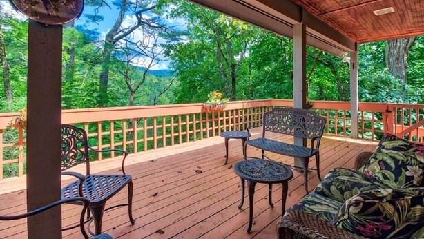 Une terrasse extérieure couverte, dotée d’un plancher en bois, de chaises en métal, d’un canapé en osier et d’une rambarde en bois.