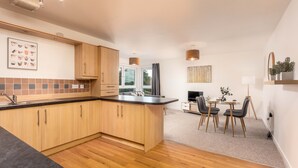 Een moderne keuken met houten kastjes, een zwart aanrecht en een eethoek met tafel en stoelen.