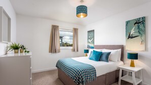 Een slaapkamer met een bed, nachtkastjes, een raam, gordijnen, een hanglamp en wanddecoratie.