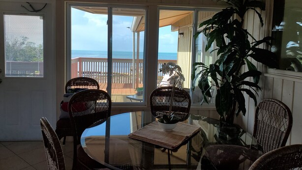 A sunlit room with a glass table, wicker chairs, and a large potted plant. - Beautiful Waterfront Large Private Gulfside Home Family Friendly.  (Marathon)