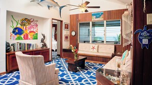 Een kamer met een blauw patatoffloor, houten meubels, een plafondventilator en een grote muurschildering van vissen.