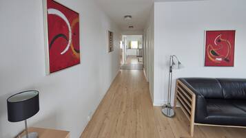 A hallway with a wooden floor, a black leather sofa, and two abstract paintings on the walls.