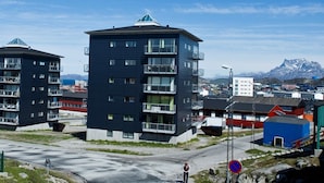 A modern building with multiple balconies, a clear sky, and a mountainous backdrop. - Nuuk Hotel Apartments by HHE (Nuuk)