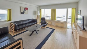 A modern living room with a black leather sofa, a wooden coffee table, a black armchair, and a TV on a wooden cabinet. - Nuuk Hotel Apartments by HHE (Nuuk)