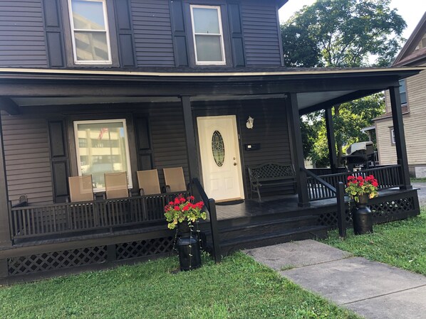 A dark-colored house with a covered porch, a front door, and two potted plants with red flowers.