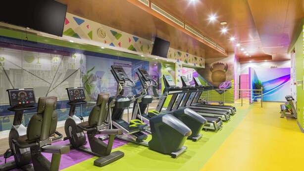 Ein Fitnessstudio mit Laufbändern, Ergometer und einer großen Wanduhr.