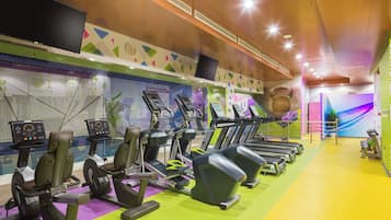 Uma academia com esteiras, bicicletas ergométricas e um relógio grande na parede.