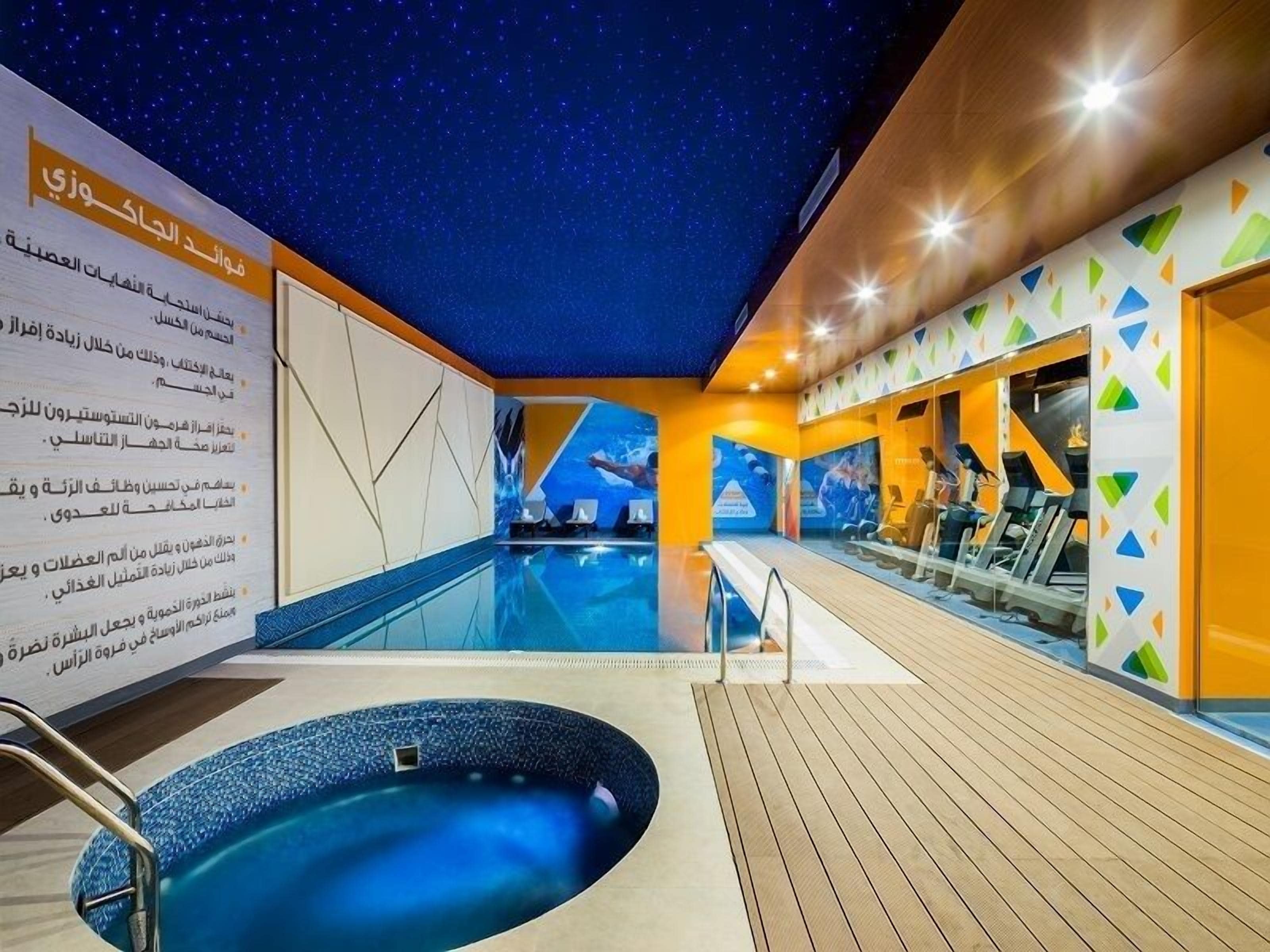 A swimming pool area with a starry ceiling, a hot tub, and exercise equipment.