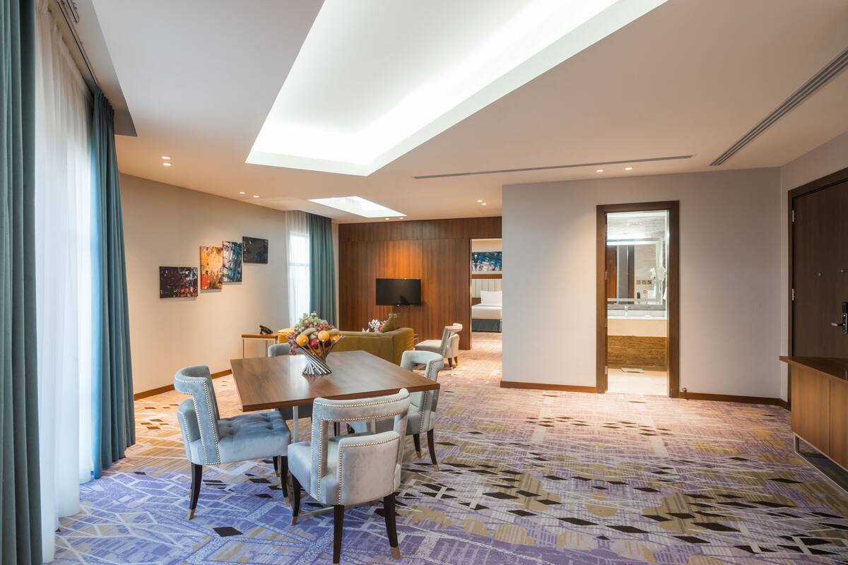 Une chambre d’hôtel dotée d’une grande table à manger, de sièges confortables, d’un téléviseur à écran plat et d’une moquette à motifs.