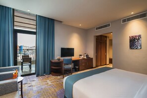Una camera d'albergo con un letto, una scrivania, una sedia, una televisione e vista all'esterno.