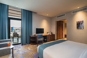 A hotel room with a bed, a desk, a chair, a television, and a view of the outside.