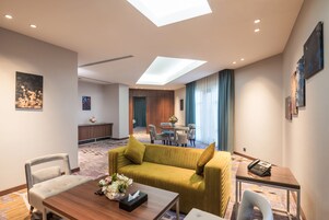 A hotel room with a sofa, a dining table, a small table with a phone, and a view of the dining area.