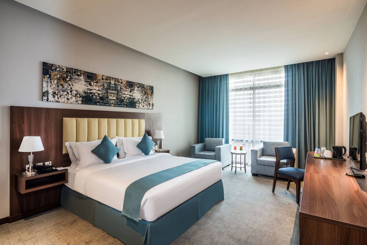 Une chambre d’hôtel avec un grand lit, un bureau, une chaise, une petite table et un téléviseur.