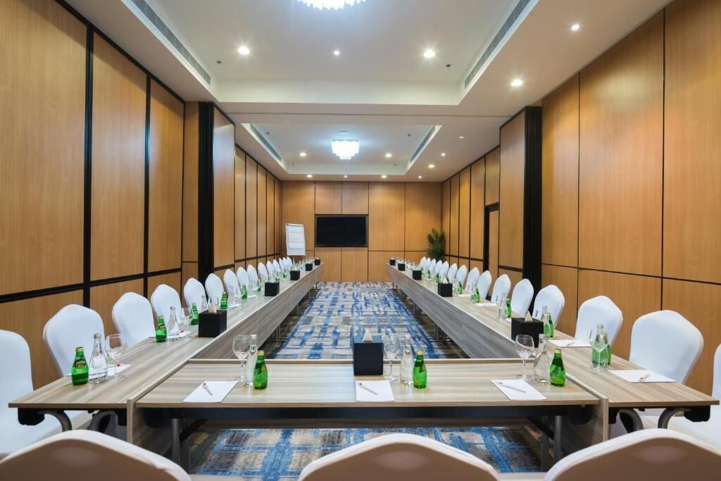 Une salle de conférence avec une longue table, des chaises blanches et un écran de projection.
