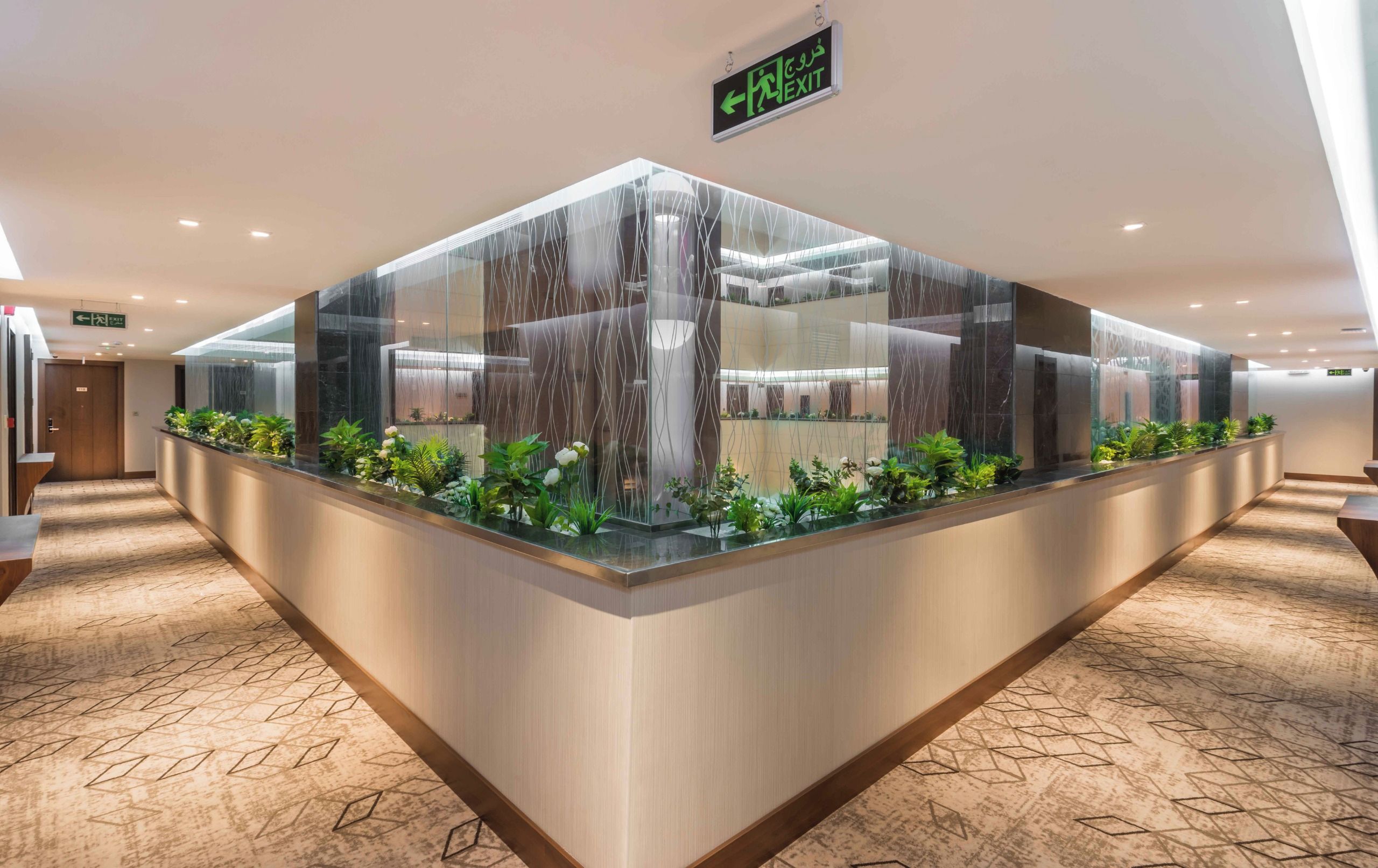 A reception area with a glass partition, plants, and an exit sign.