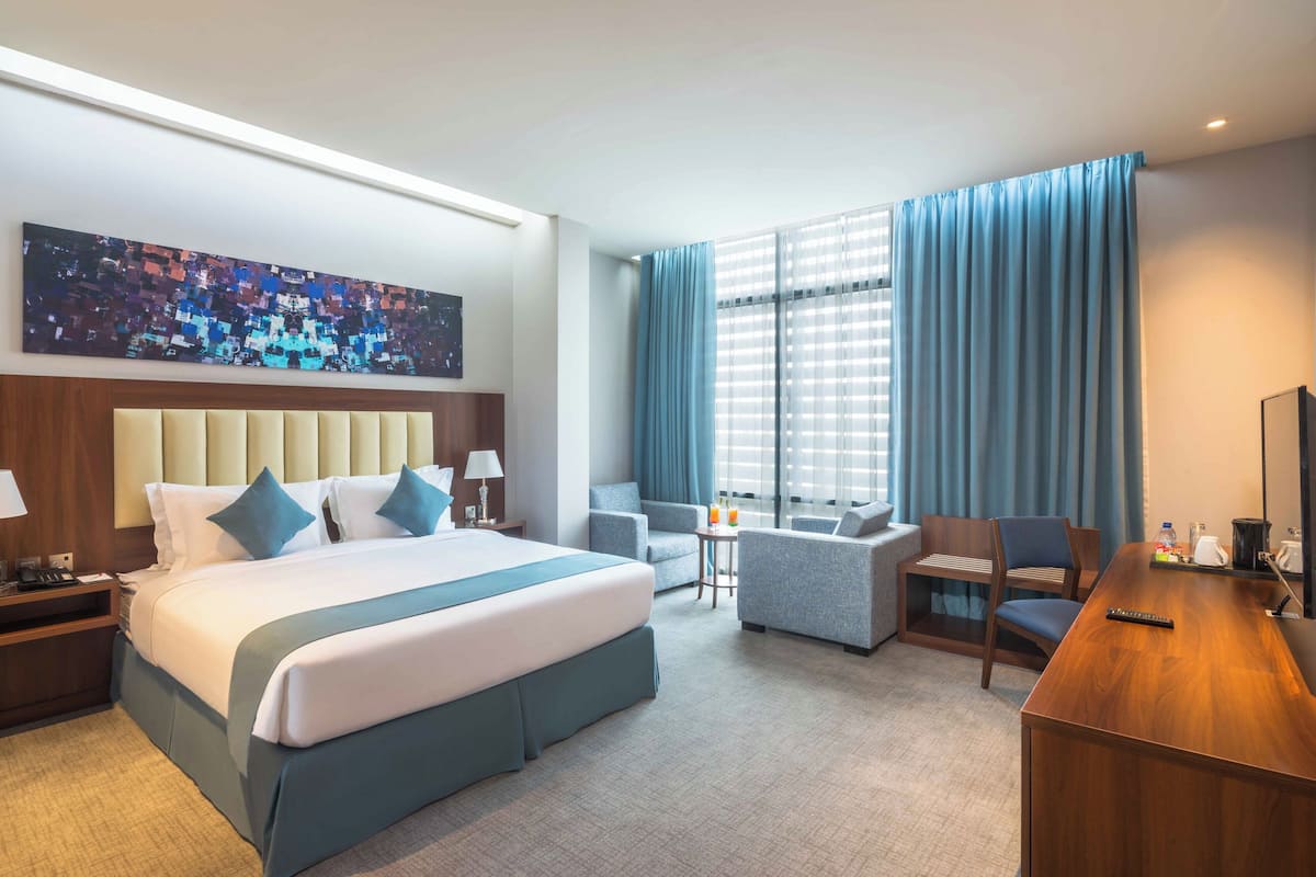 Une chambre d’hôtel avec un grand lit, un bureau, une chaise, un canapé et une fenêtre avec des rideaux.