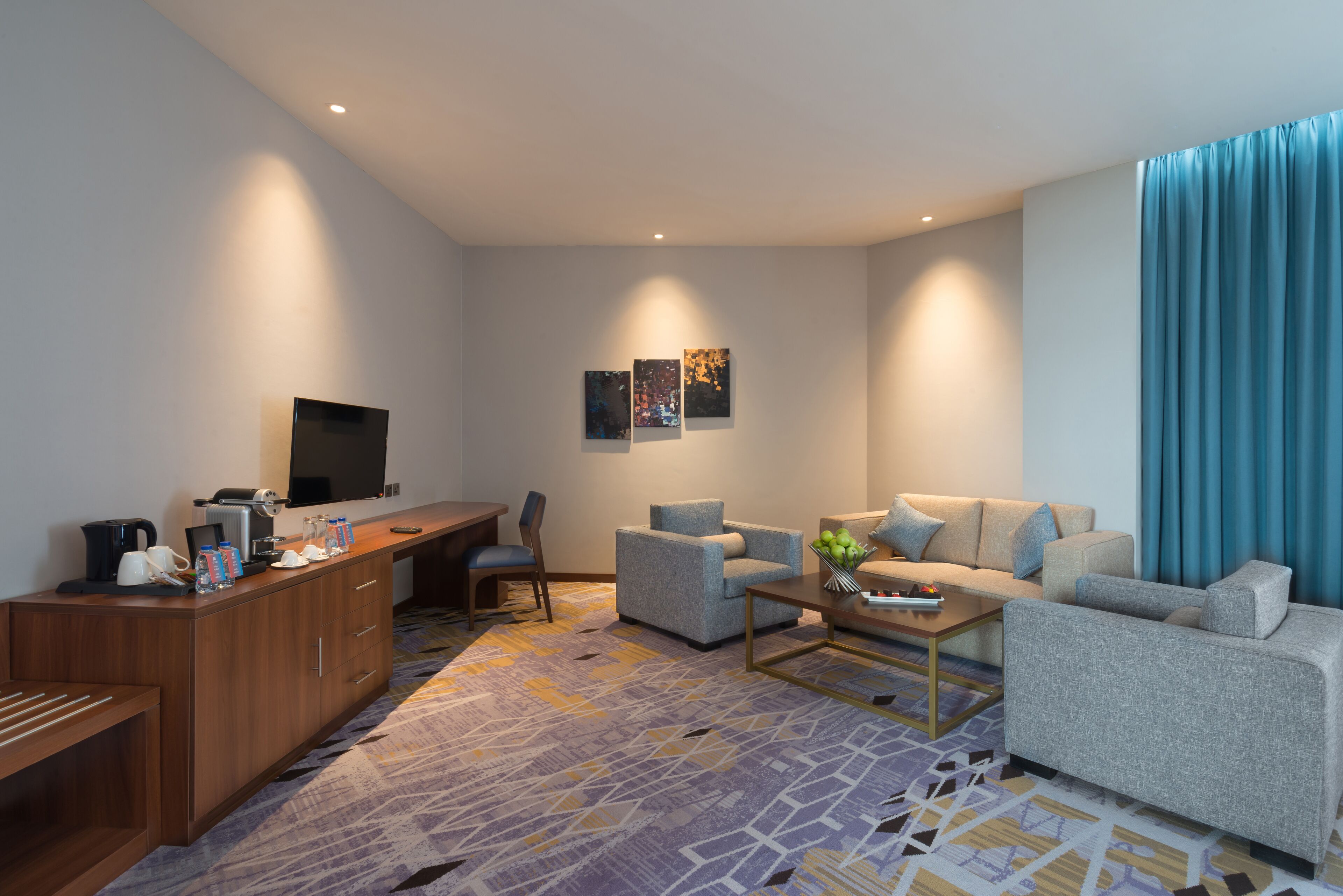 A modern living room with a sofa, armchair, coffee table, and a flat-screen TV mounted on the wall.