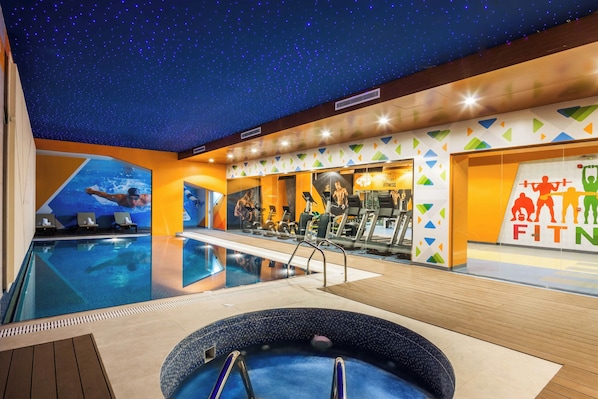 A swimming pool with a starry ceiling, a hot tub, and a fitness center with exercise equipment.