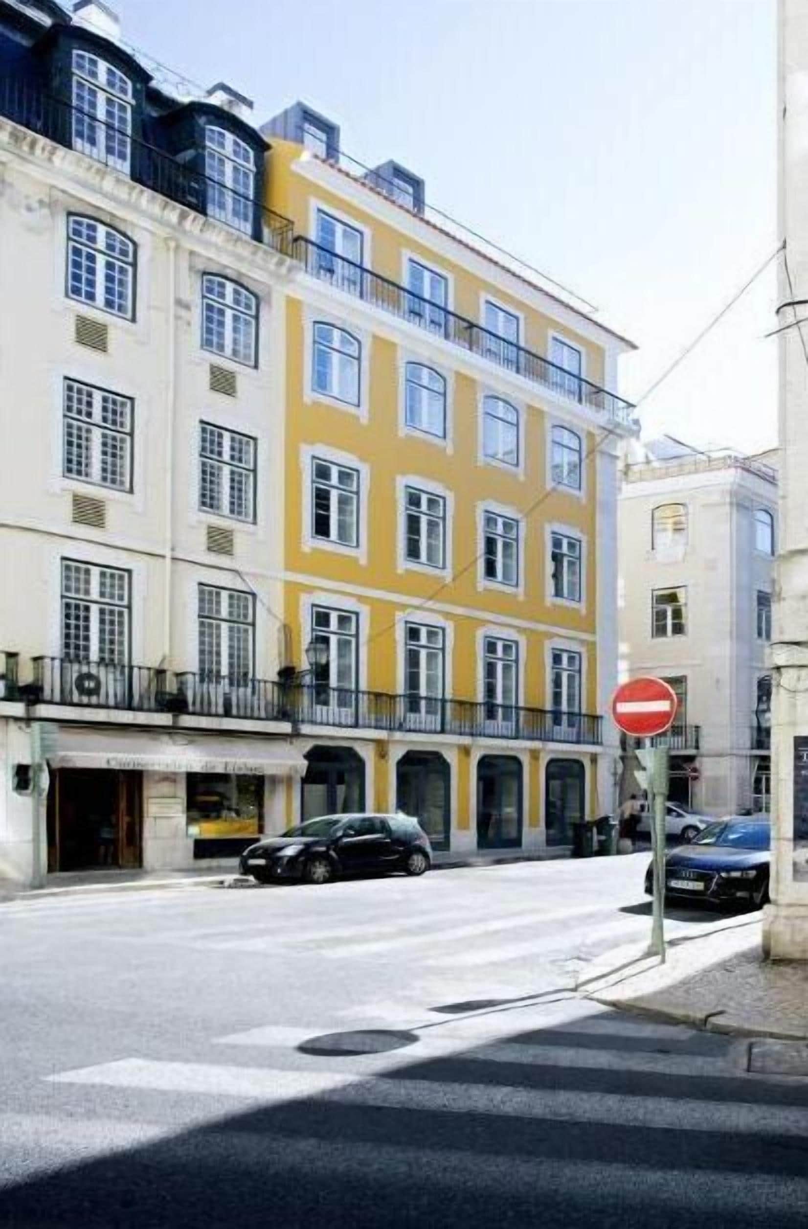 A street view with a row of colorful buildings, a no entry sign, and parked cars.