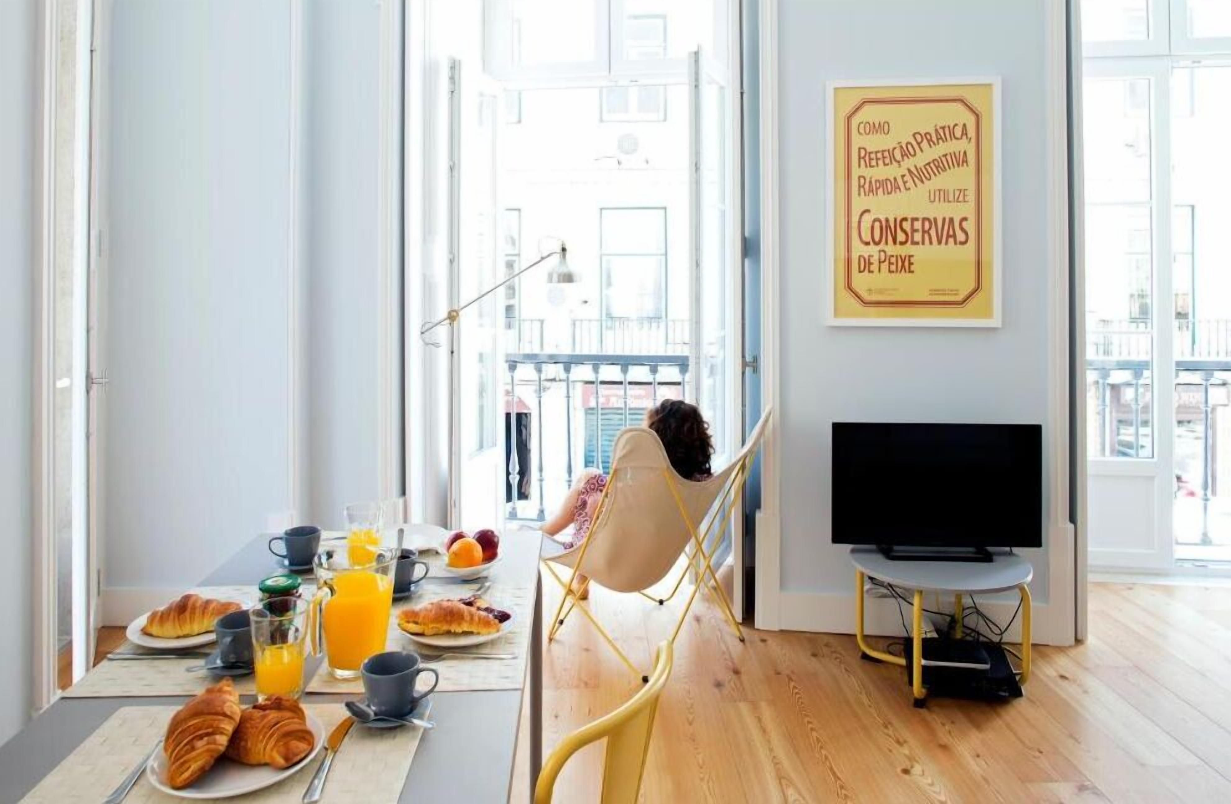 A breakfast setup with croissants, orange juice, and a TV in a bright room with a balcony view.