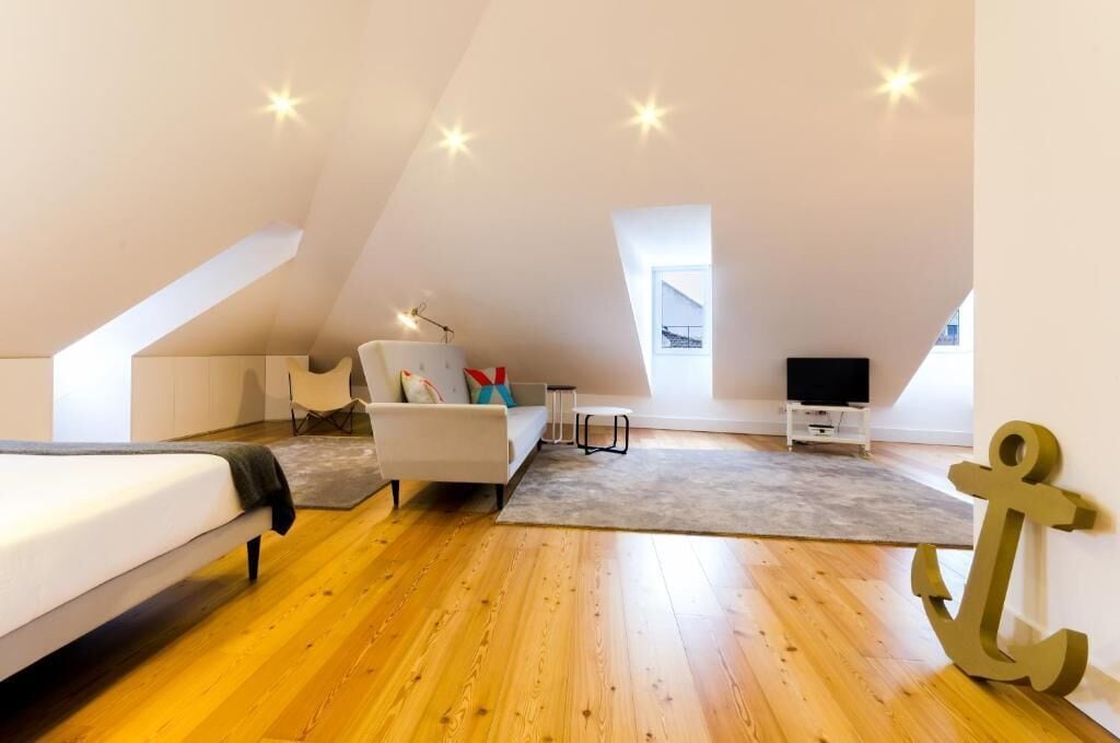 Un dormitorio tipo loft moderno con techo inclinado, suelo de madera, una cama, un sofá blanco, una mesita, un televisor y una gran decoración con forma de ancla.