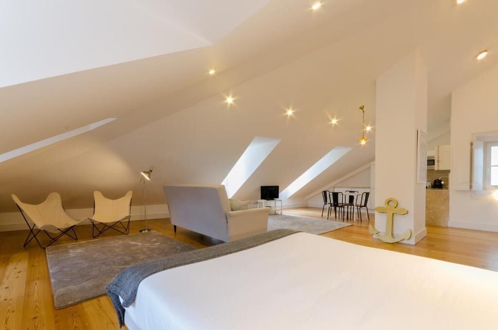 A spacious attic bedroom with a large bed, two chairs, a desk, and a dining area.