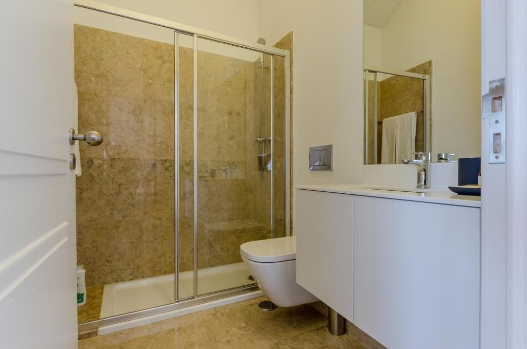 Une salle de bain avec une douche à parois de verre, des toilettes blanches et un grand miroir au-dessus du lavabo.