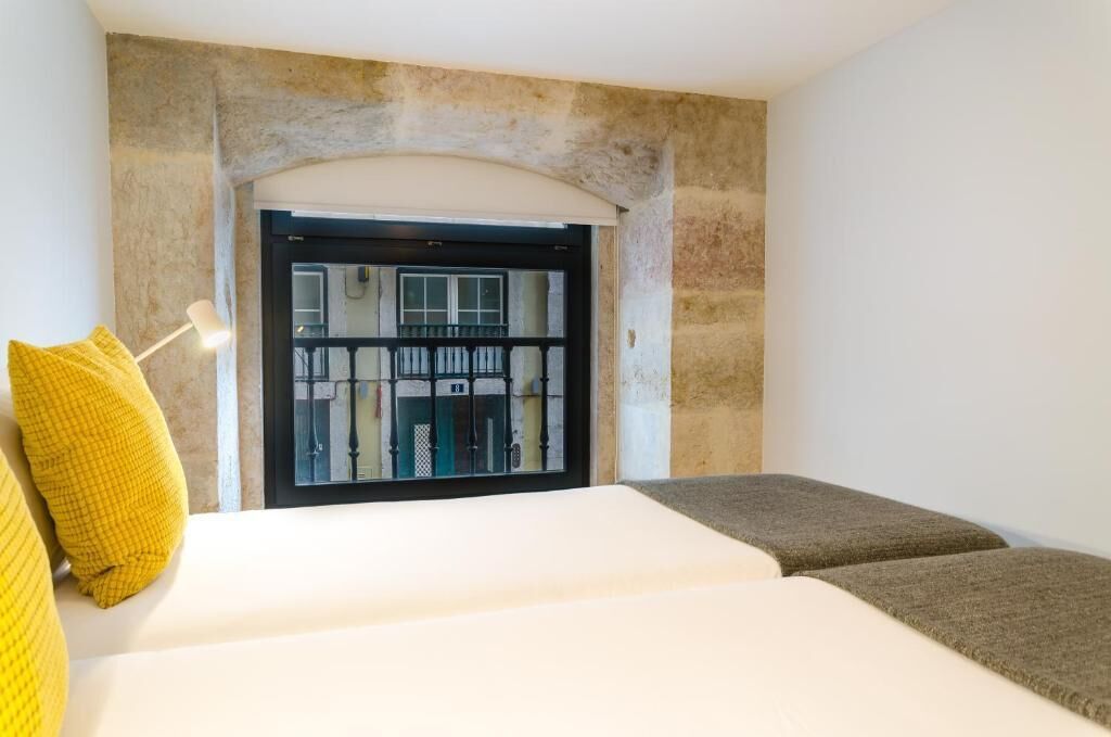 Een kamer met een bed, een raam met uitzicht op een gebouw en een stenen muur.