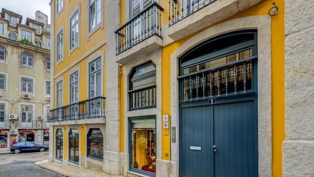 Ein Gebäude mit gelber Fassade, einer dunkelblauen Tür und einem Balkon mit schwarzen Geländern.