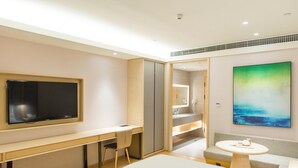 A modern hotel room with a large bed, a desk with a chair, a television, a bathroom with a mirror, and a painting on the wall. - Jinjiang Inn Style (Fuzhou)